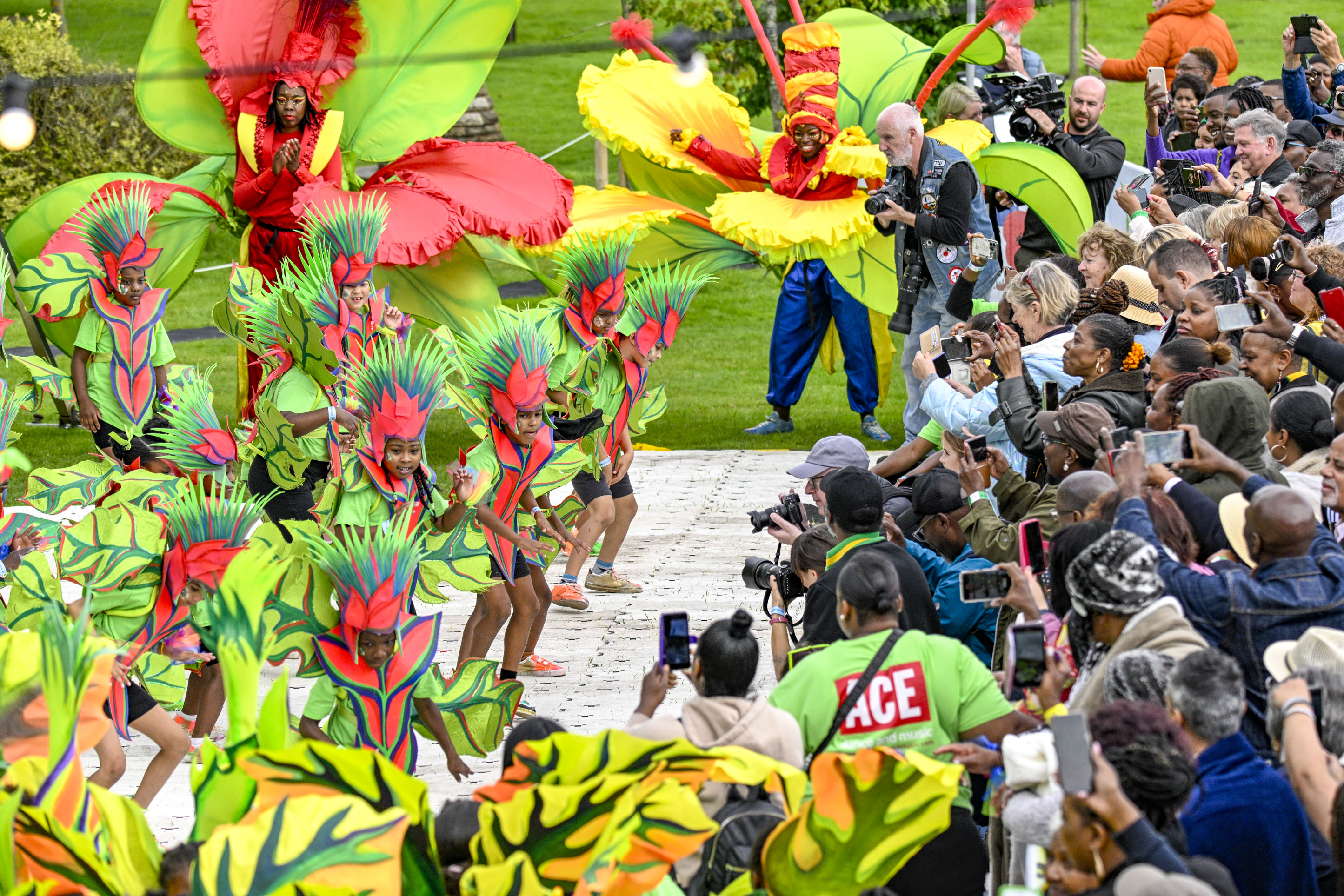 Image shows a crowd of young people in red and green carnival dress performing in front of a crowd