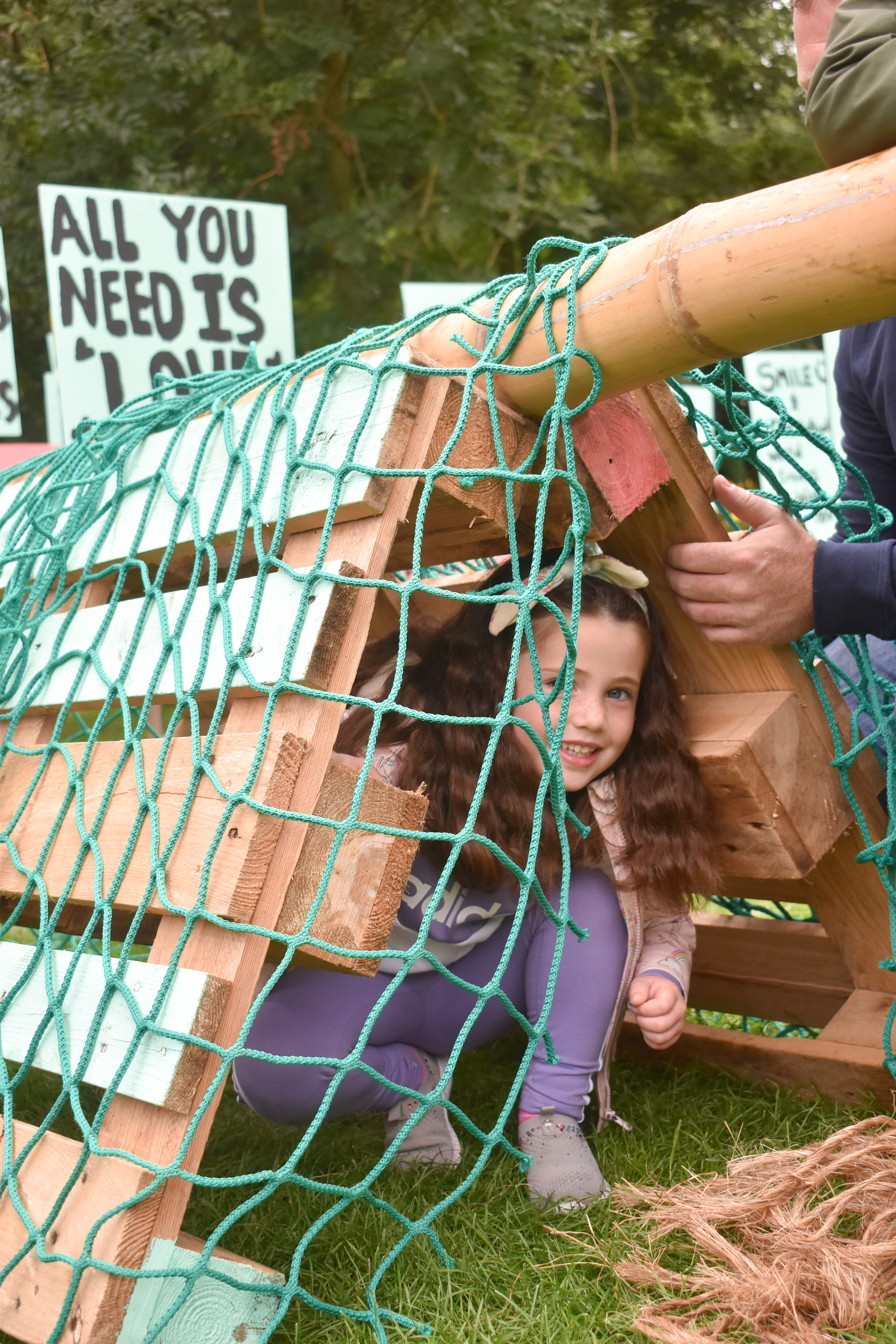 A young girl peers out of den created using pallets and net